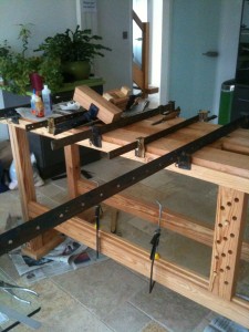 Shows the bench being glued in the kitchen and shows clearly the sliding leg to support long planks in the vice.